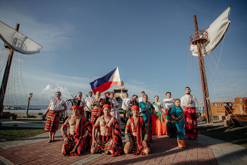 A group performing cultural dance in traditional attire by the waterfront, showcasing heritage and identity.